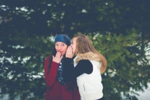 ignore the noise
teen girls in winter vest whispering to one another in front of a large pine tree