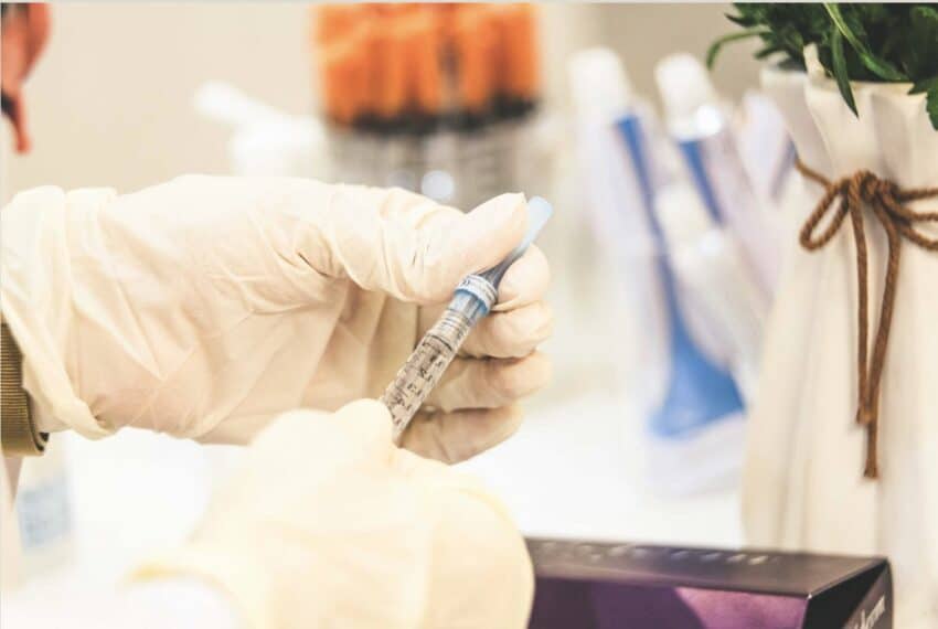 gloved hands holding a medical syringe with medical supplies in the background